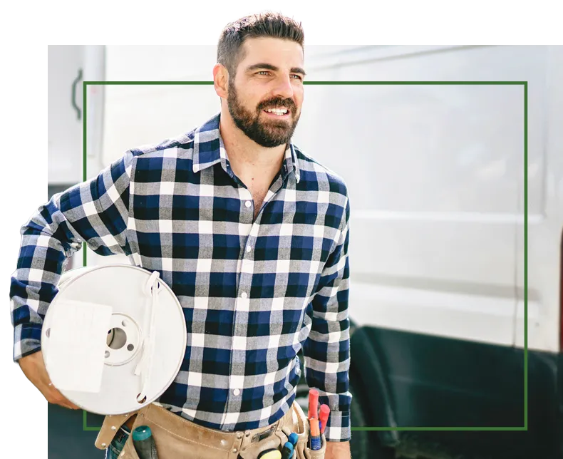 Handyman in plaid shirt holding cable reel, standing by a van.